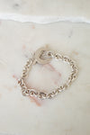 A silver chain link bracelet with a toggle clasp, sitting on a marble surface. 