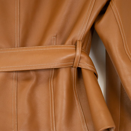 Close-up of a tan leather jacket with a matching waist belt, showing the texture, stitching, and sleeve detail against a white background.