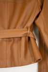 Close-up of a tan leather jacket with a matching waist belt, showing the texture, stitching, and sleeve detail against a white background.