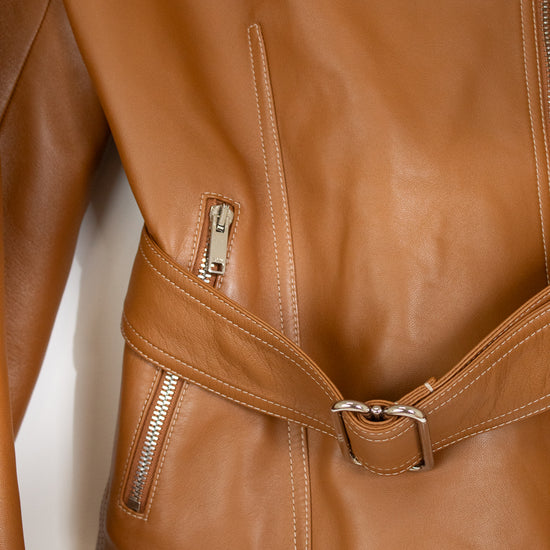 Close-up of a tan leather jacket showing the side zip pocket, belt detail with silver buckle, and zipper on a plain white background.