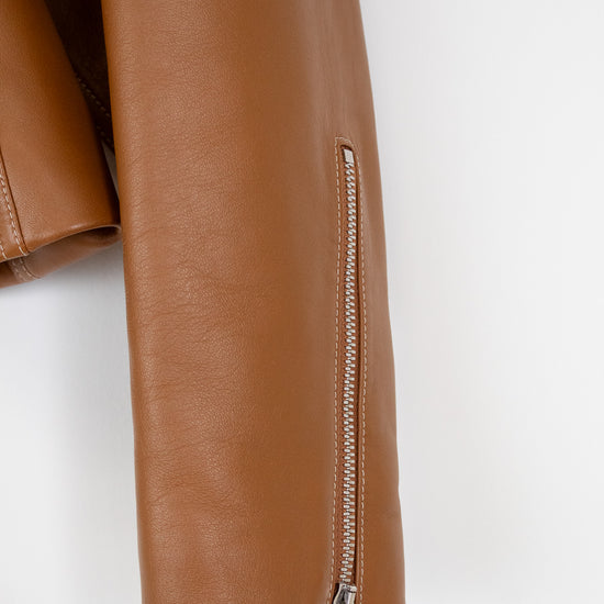 Close-up of a tan faux-leather jacket sleeve featuring a vertical zippered detail with a silver zipper pull, set against a plain white background.