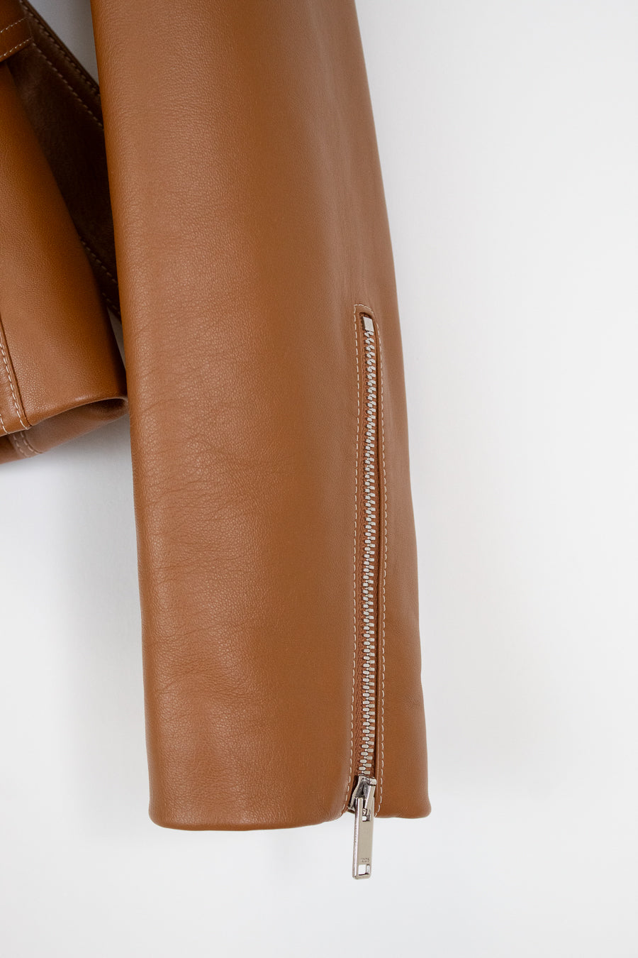 Close-up of a tan faux-leather jacket sleeve featuring a vertical zippered detail with a silver zipper pull, set against a plain white background.
