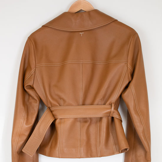 A tan leather jacket with a collar and matching waist belt, hanging on a wooden hanger against a plain white wall.