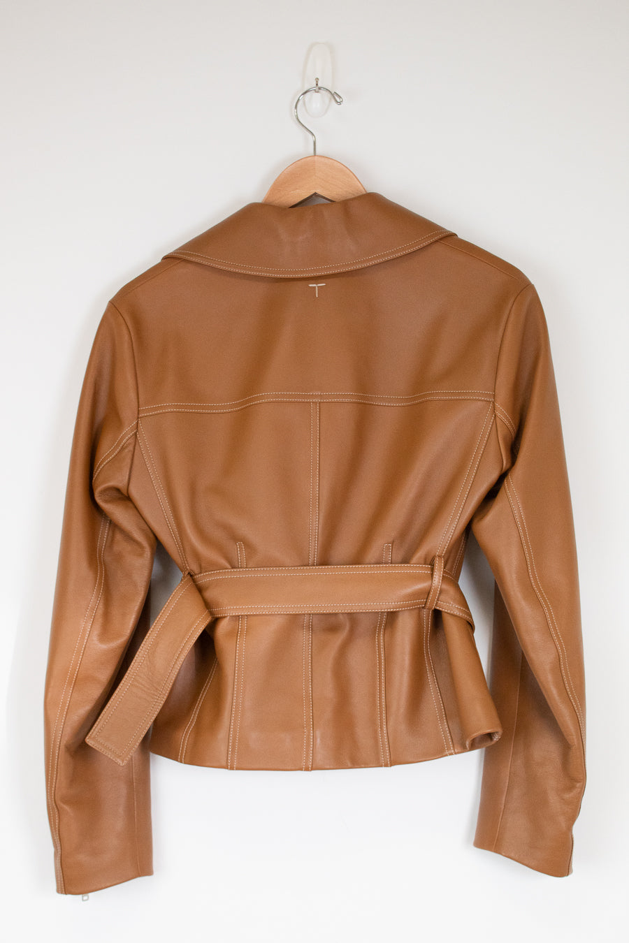 A tan leather jacket with a collar and matching waist belt, hanging on a wooden hanger against a plain white wall.