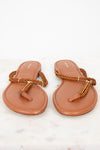 A pair of tan leather thong sandals with braided brown straps and gold-tone hardware, displayed on a white marble surface against a white background.