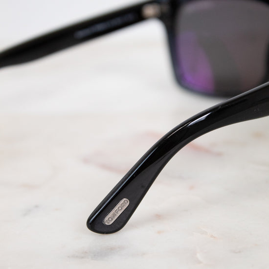 Black sunglasses with a brand logo on a light marble surface