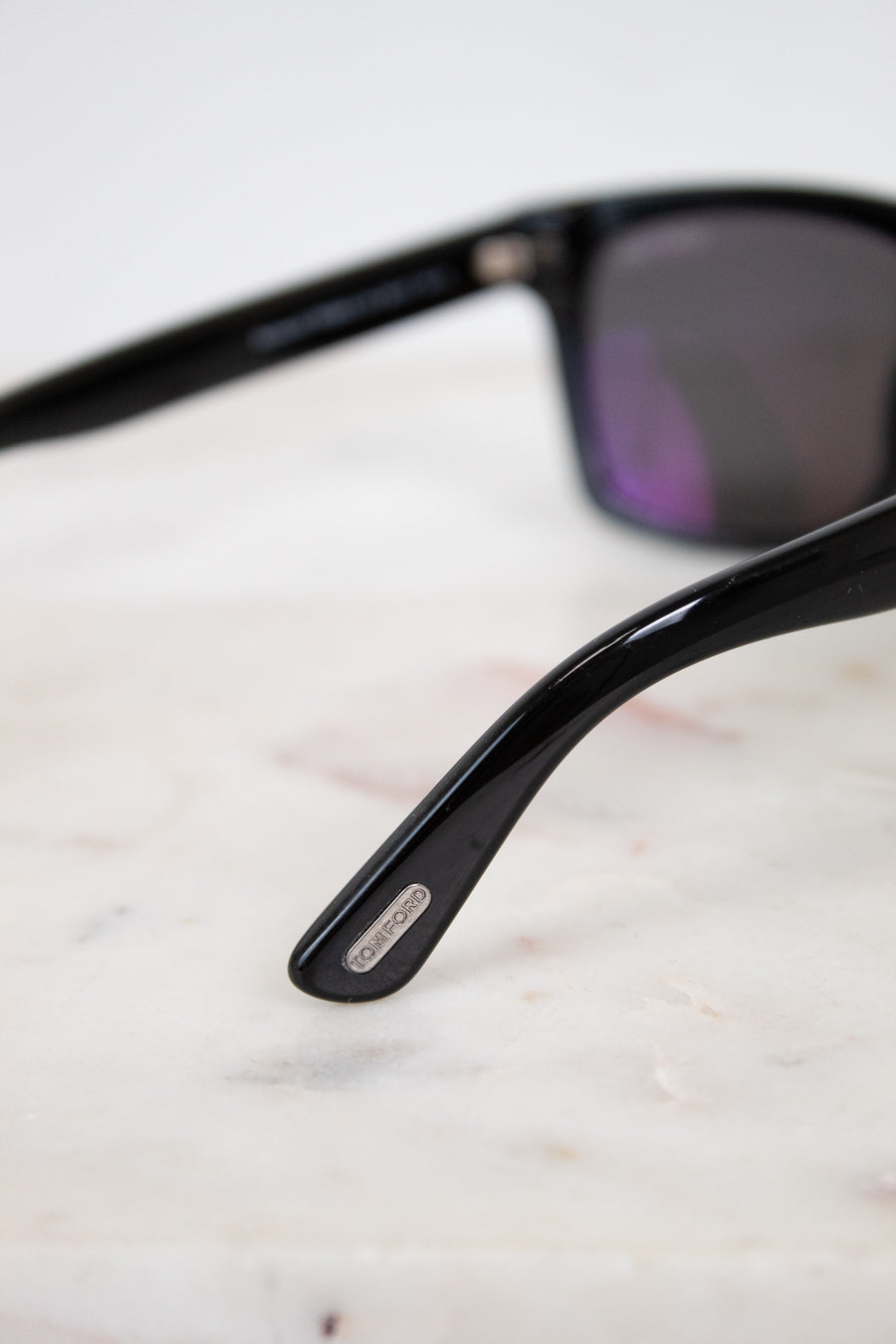 Black sunglasses with a brand logo on a light marble surface