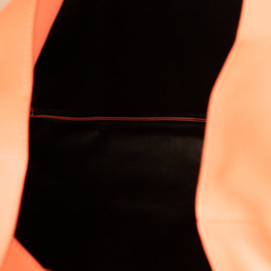 Close-up of a bright coral orange bag with a black interior lining and a thin red accent line.