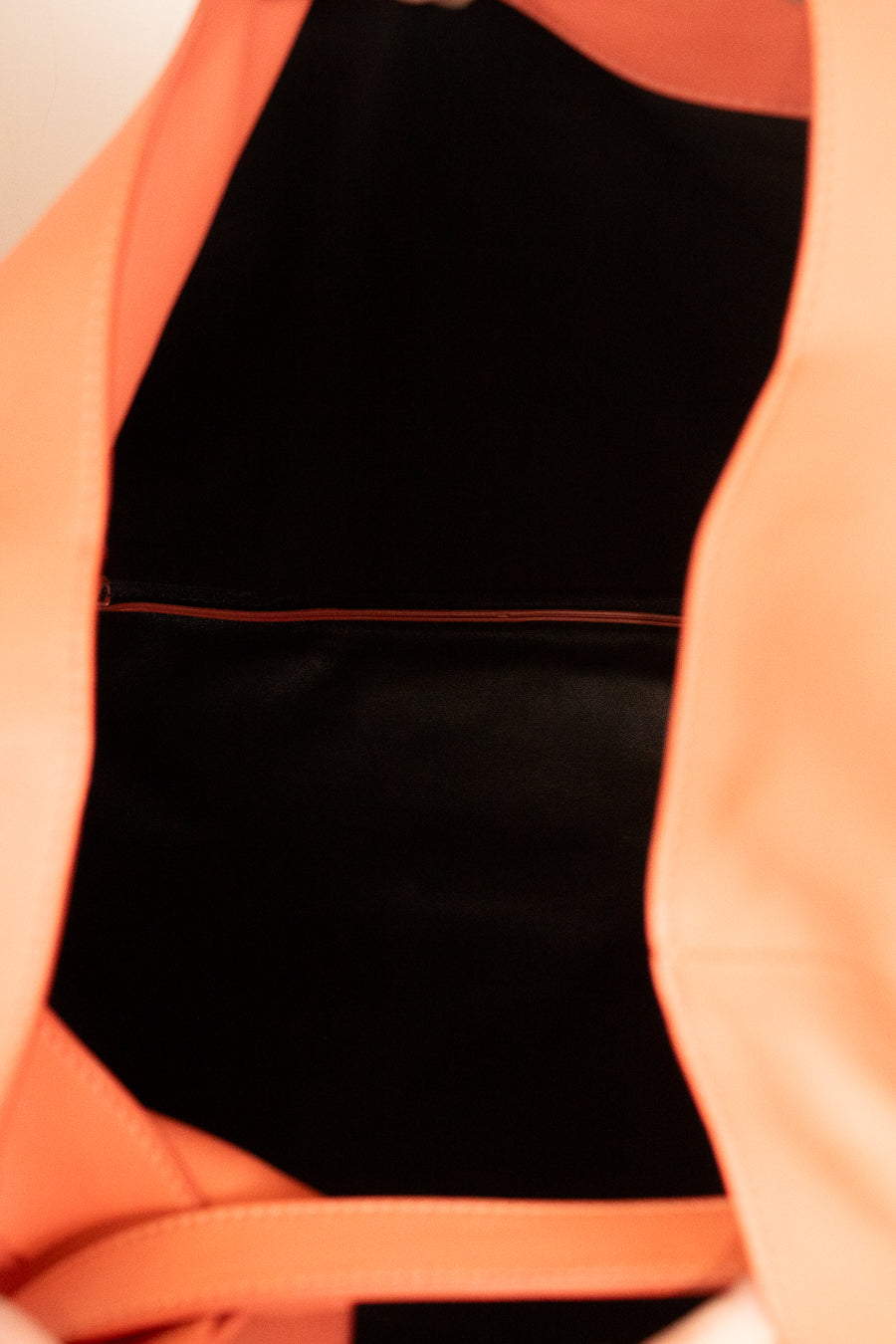Close-up of a bright coral orange bag with a black interior lining and a thin red accent line.