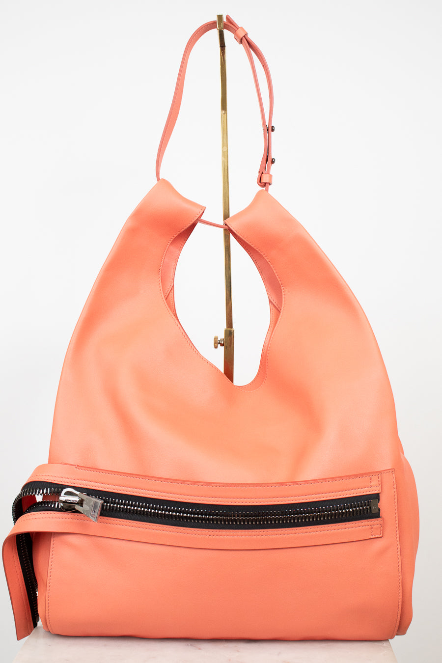 A coral orange leather shoulder bag with a front zippered pocket and a gold-tone metal stand, photographed against a plain white background.