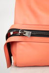 Close-up of a coral orange leather bag with a black zipper and a silver-toned metal slider pull featuring the 'Tory Ford' brand name.