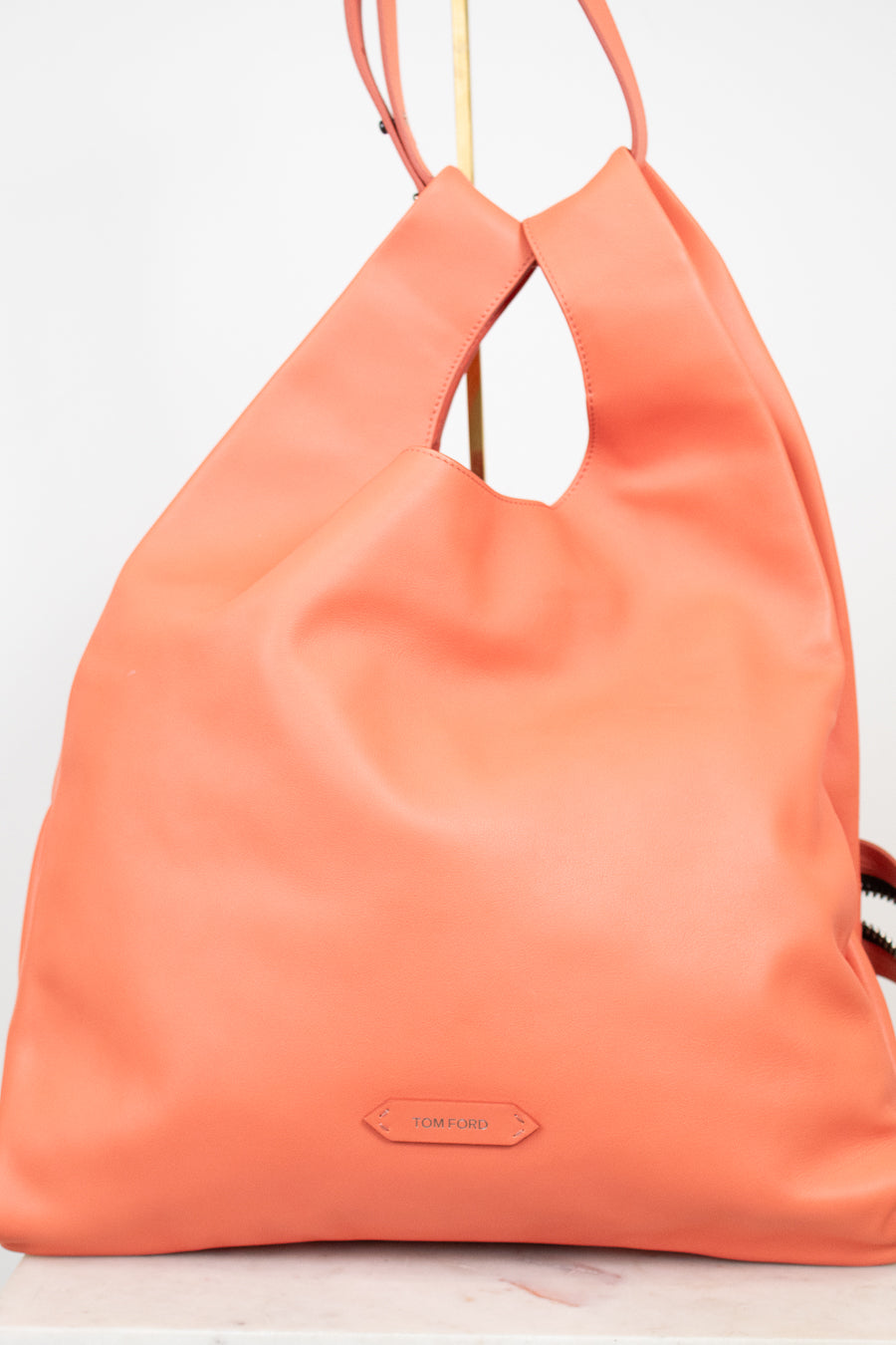 A coral orange leather slouchy shoulder bag with a cutout top and a small 'TOM FORD ' brand plaque on the front, displayed on a white background.