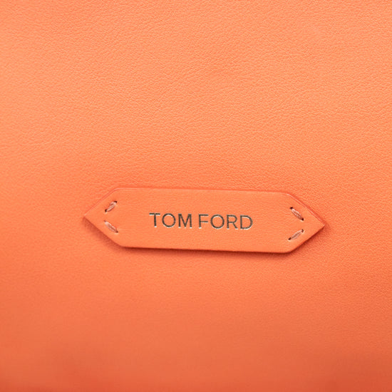 Close-up of a textured orange leather bag with a central tan leather brand tab reading TOM FORD.