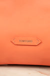 Close-up of a textured orange leather bag with a central tan leather brand tab reading TOM FORD.