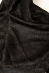 A close-up of draped black fabric with a subtle glittery texture against a white background visible at the top edge.