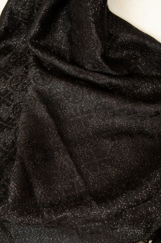 A close-up of draped black fabric with a subtle glittery texture against a white background visible at the top edge.