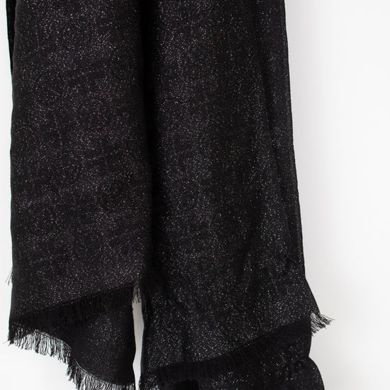 A close-up of a black textured scarf with fringed edges, draped against a plain white background.