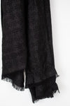 A close-up of a black textured scarf with fringed edges, draped against a plain white background.