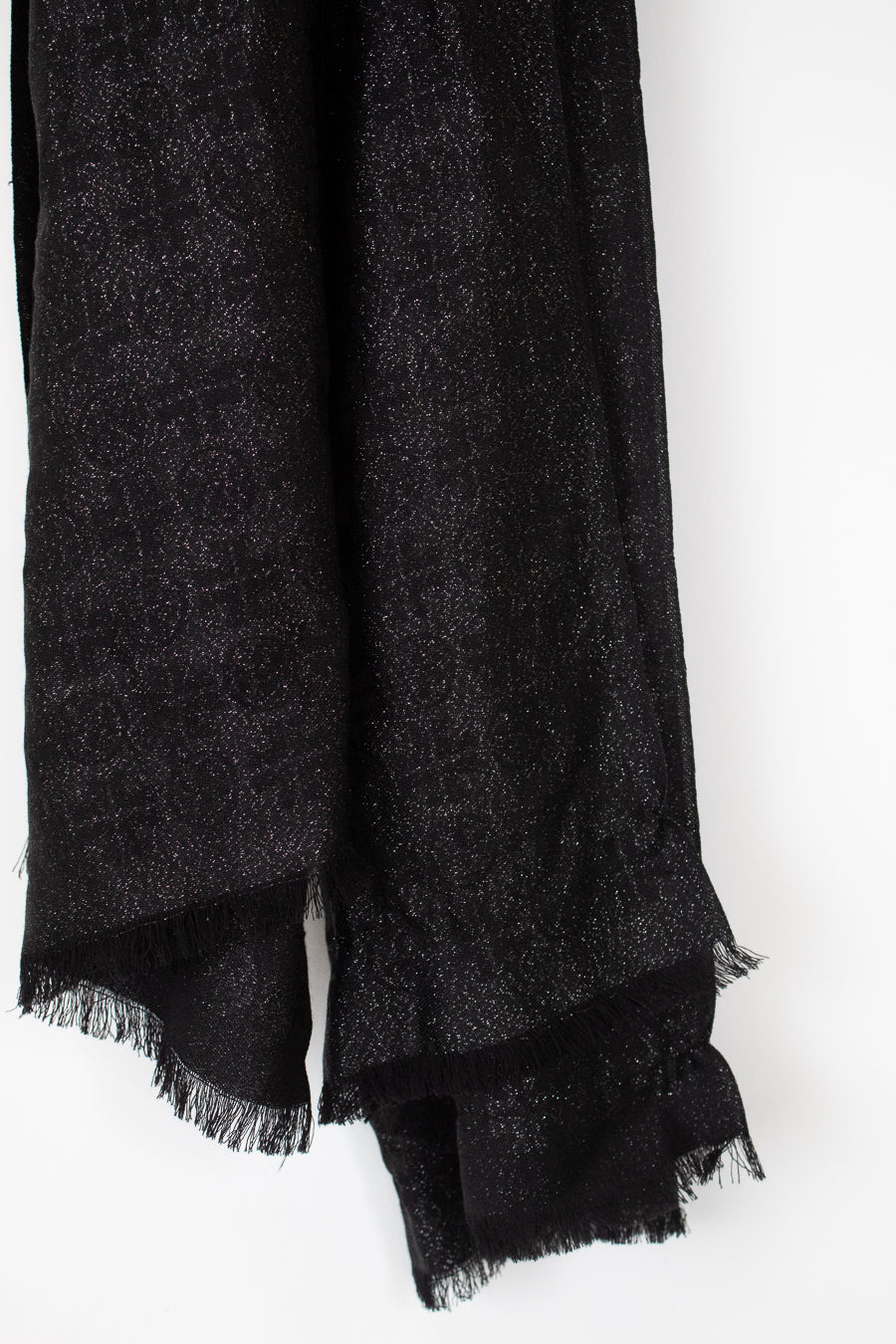 A close-up of a black textured scarf with fringed edges, draped against a plain white background.
