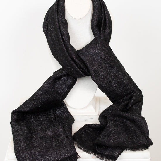 A black textured scarf with subtle shimmer and fringed edges, draped on a white canvas bust against a plain white background.