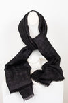 A black textured scarf with subtle shimmer and fringed edges, draped on a white canvas bust against a plain white background.