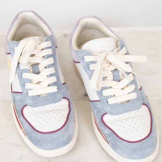A pair of low-top sneakers in light blue suede and white leather, featuring white laces, a white heart-shaped toe overlay, and thin red piping details, displayed on a white marble surface.