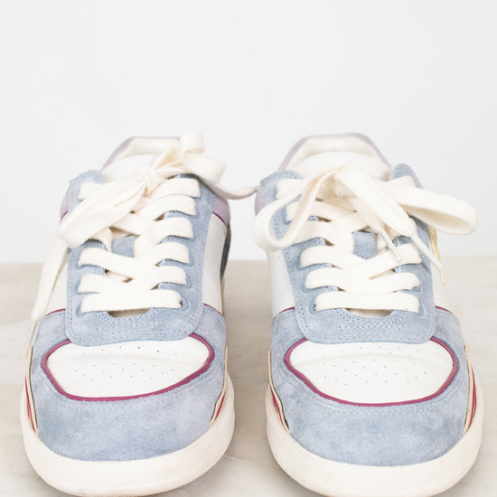A pair of light blue suede sneakers with white leather panels, white laces, and thin red and orange piping details, displayed on a white marble surface against a white background.