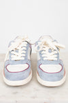 A pair of light blue suede sneakers with white leather panels, white laces, and thin red and orange piping details, displayed on a white marble surface against a white background.