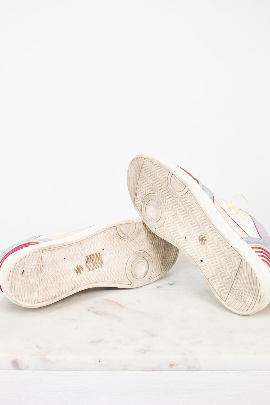 A pair of low-top sneakers shown from the sole side, resting on a light marble surface against a white background.