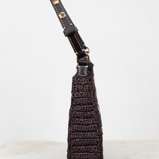 Brown woven purse with brown strap on a light gray background