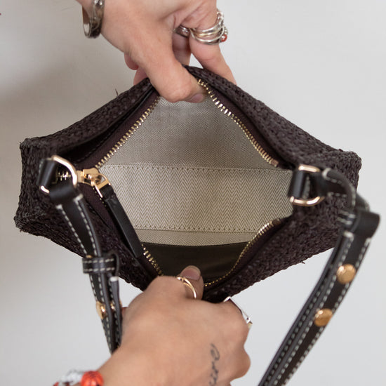 Person holding brown woven purse with dark brown leather straps open showing clean interior