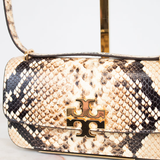 A close-up of a handbag with beige, black, and brown snakeskin leather, featuring a gold-tone metal logo clasp on the front flap.