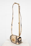 A snakeskin leather shoulder bag with a long matching strap on a gold-tone metal stand, displayed on a white marble surface against a white background.