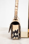A close-up side view of a snakeskin leather handbag,  featuring a gold-tone metal frame and strap attachment, set against a clean white background.