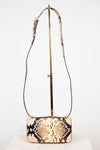 A snakeskin leather shoulder bag with a rectangular body and long matching  strap, displayed on a gold stand against a white background.