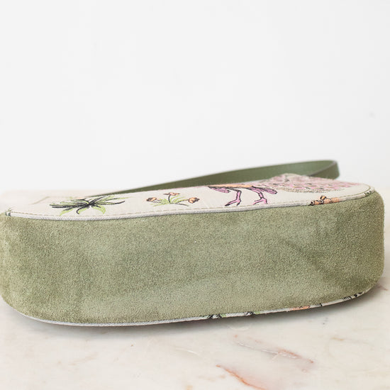 An olive green velvet shoe bag with a floral-patterned fabric top panel, resting on a white marble surface against a white background.