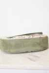 An olive green velvet shoe bag with a floral-patterned fabric top panel, resting on a white marble surface against a white background.
