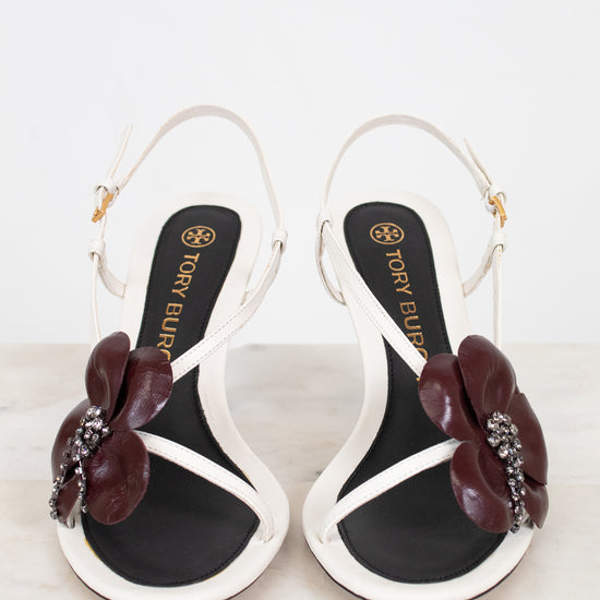 Pair of black and white sandals with floral embellishments on a light background