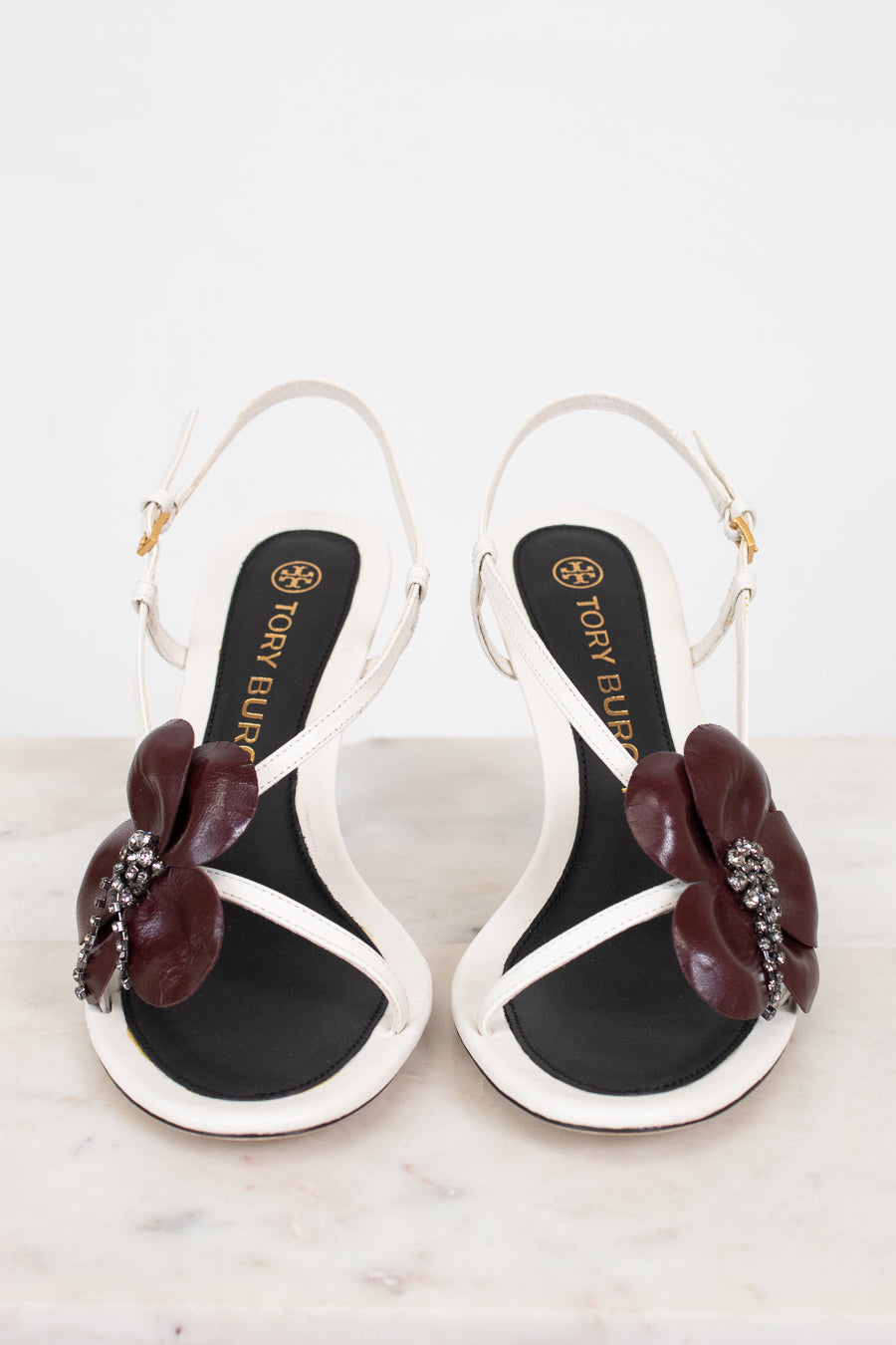 Pair of black and white sandals with floral embellishments on a light background