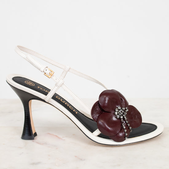 White sandal with a gold buckle and maroon flower detail on a white background