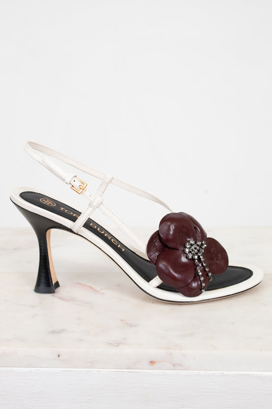 White sandal with a gold buckle and maroon flower detail on a white background