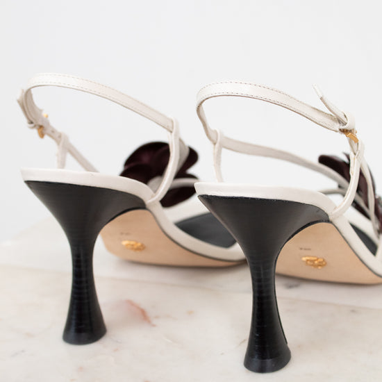 White strappy high-heeled shoes with black heels on a marble surface