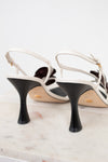 White strappy high-heeled shoes with black heels on a marble surface