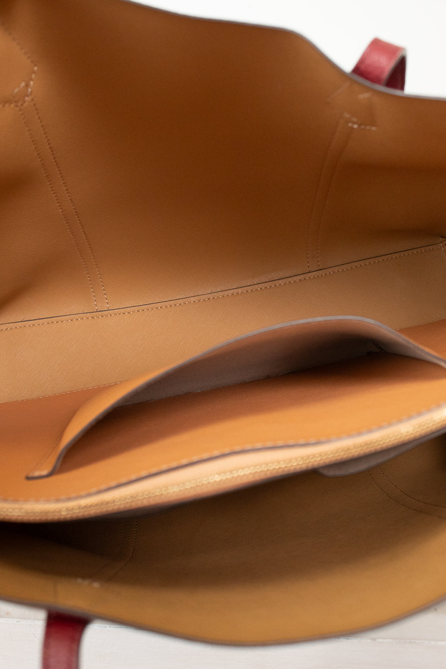 Close-up of the interior of a tan leather bag, showing stitched compartments and a small red leather strap detail at the top and bottom edges.