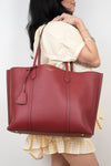 A woman wearing a yellow and white gingham dress carries a large burgundy leather tote bag over her shoulder against a plain white background.