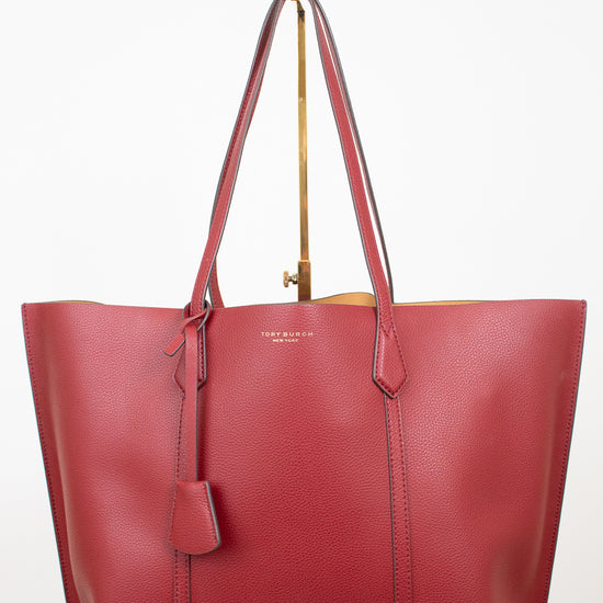 A red leather tote bag with double shoulder straps and a hanging leather tag, displayed on a gold stand against a white background.