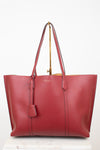 A red leather tote bag with double shoulder straps and a hanging leather tag, displayed on a gold stand against a white background.