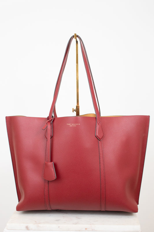 A red leather tote bag with double shoulder straps and a hanging leather tag, displayed on a gold stand against a white background.