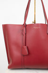 A red pebbled leather tote bag by Tory Burch, featuring dual shoulder straps, a hanging leather tag, and gold-tone hardware, shown against a clean white background.