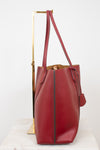 A red pebbled leather tote bag with double shoulder straps, displayed on a gold metal stand against a white background.